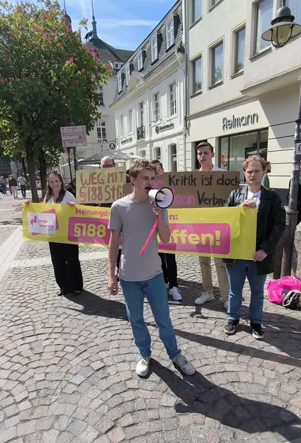 Ein Teilnehmer spricht mit einem Megafon zu den Demonstrierenden, während die Jungen Liberalen Rhein-Erft und Rhein-Sieg mit Plakaten und Bannern in der Brühler Innenstadt gegen den Paragrafen 188 des Strafgesetzbuches protestieren.  | Foto: Junge Liberale Rhein-Erft