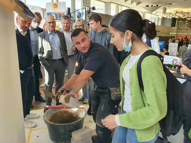 Realschülerin Erif Cüngür lässt sich von Maurerlehrling Resad Bibic zeigen, wie das Handwerk funktioniert, während unter anderem Oberbürgermeister Uwe Richrath (im Hintergrund von links), Wupsi-Geschäftsführer und Vorsitzender der Unternehmerschaft Rhein Wupper Marc Kretkowski, Andreas Tressin und Eva Babatz zu schauen.  | Foto: Gabi Knops-Feiler