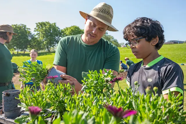Gartenmeister Julian Bikker erklärt den Schulkindern, wie die Sommerblumen am besten ausgetopft werden. | Foto: Sascha Engst/Bundesstadt Bonn