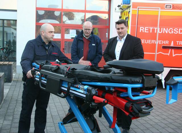 Ein Mitarbeiter der Feuer- und Rettungswache (l.) erklärt Bürgermeister Alexander Biber und dem Beigeordneten Horst Wende (v.r.) die Funktionsweise der elektrohydraulischen Fahrtrage.