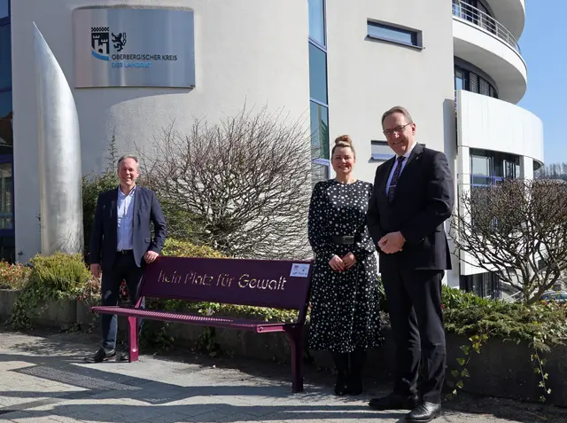Landrat Jochen Hagt (r.), Kreisdirektor Klaus Grootens und die Gleichstellungsbeauftragte des Oberbergischen Kreises, Magdalena Tertel, neben der Motivbank „Kein Platz für Gewalt“ am Haupteingang des Kreishauses in Gummersbach.  | Foto: OBK
