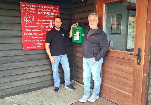 Thomas Körfer und Joachim Kurz mit dem lebensrettenden Defibrillator am Eingang zum Dorfhaus.  | Foto: Regina Wendscheck
