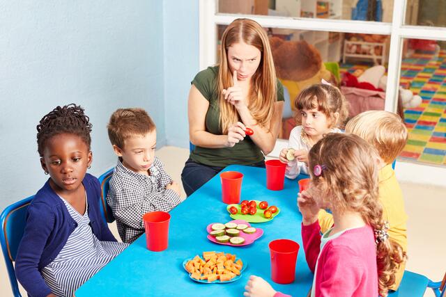 Eine Betreuerin zusammen mit Kindern beim Essen.  | Foto: Robert Kneschke@stock.adobe.com