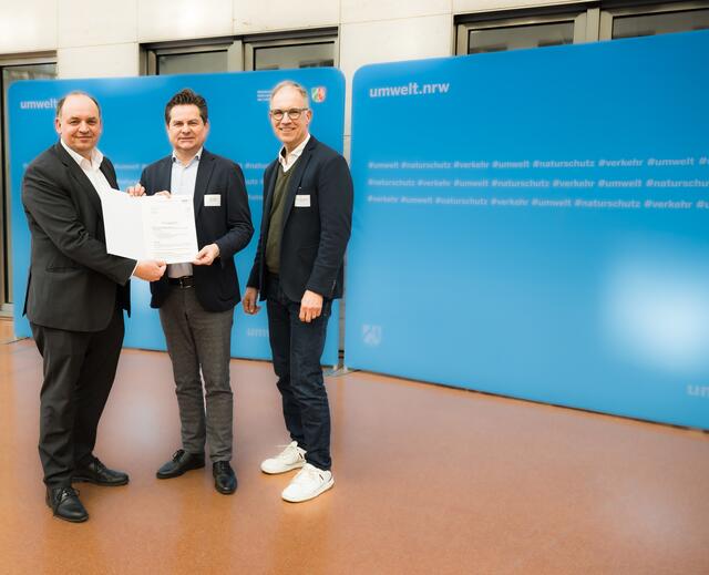 Staatssekretär Viktor Haase (l.) überreicht den Förderbescheid an Bürgermeister Ulrich Stücker, begleitet von VRS-Geschäftsführer Dr. Norbert Reinkober (r.).  | Foto: MUNV NRW