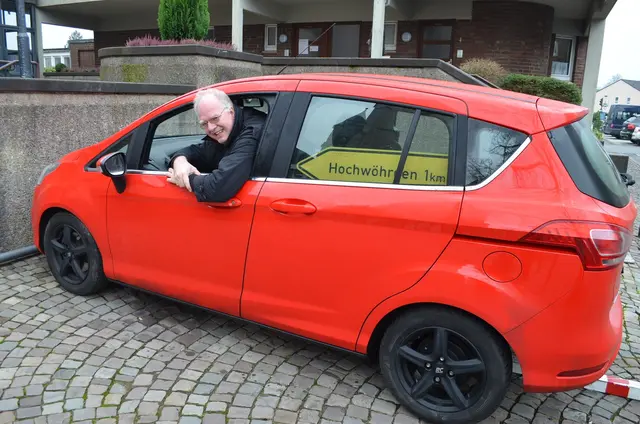 Hochwürden Christoph Bersch mit dem Hinweisschild auf die Ortschaft Hochwöhrden (Norddeutschland) im Auto.  | Foto: Archivfoto: Franke