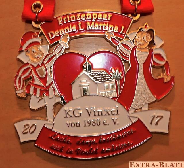 Prinzenpaar der KG Vinxel - Den Sessionsorden der KG Vinxel 1980 e.V. hat Prinz Dennis I. persönlich entworfen. Ein Spruchband mit dem Sessionsmotto „Lache, danze, kostümiere, sich in Veußel amüsiere“ zu Füßen und die Vinxeler Marienkapelle im Herzen tanzt das Prinzenpaar, Dennis I. und Martina I., darauf um den Vünftzailplatz.  | Foto: Repro Verlag