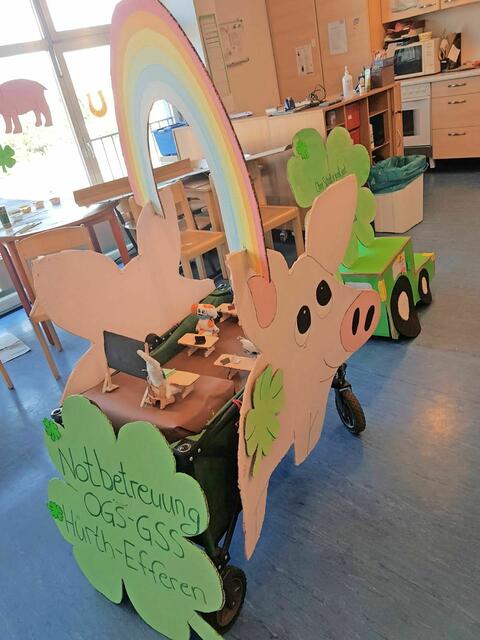 Kennziffer 04 - Die Notbetreuung der OGS der Grundschule in Hürth-Efferen hat gemeinsam  gebastelt. Das Motto des Karnevalswagens lautet: „Ohne Schull es jar nit jood, wie ne Zaubrer ohne Hoot, mer wünschen uns zu unsrem Jlöck, lasst uns in die Schull zoröck!" Kleeblätter und Schweinchen sollen Glück bringen. „Für unsere Kinder bedeutet Glück die Möglichkeit in die Schule zu gehen und mit der Lehrerin im Klassenraum gemeinsam Unterricht machen zu können und natürlich ganz besonders in den Pausen und Nachmittags mit den Mitschülern spielen zu dürfen“, schreiben die OGS-Betreuer der Geschwister-Scholl-Grundschule. Auf dem Karnevalswagen sitzen alle Schüler und Schülerinnen mit Abstand und Mundschutz genau nach Corona Vorschrift. Sie lernen gerade Mathematik. Wie man auf der Tafel sehen kann, wird gerade die wichtige Rechnung "Dreimal Null es Null es Null" gelehrt. Im Traktor sitzen viele glückliche Kinder. Sie fahren optimistisch ins Jahr 2021 in der Hoffnung auf die Erfüllung ihrer Träume. Der "Alles wird gut-Regenbogen" überspannt den Wagen. Vorne auf dem Traktor ist ein Zauberhut zu sehen, aus dem eine Schule gezaubert wird. Der Zauberhut soll das Schulministerium symbolisieren, das die "magische Fähigkeit" besitzt Präsenzunterricht "herzuzaubern". | Foto: OGS Grundschule Efferen