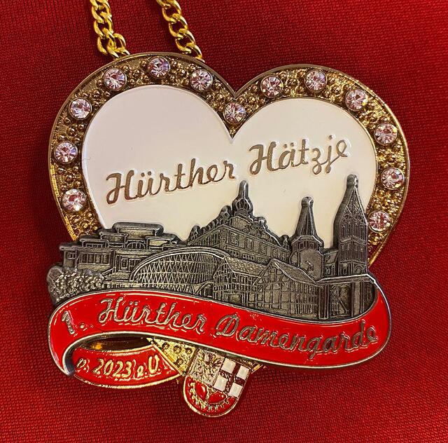 1. Hürther Damengarde von 2023 - Hürther Hätzje e.v.
Der selbst entworfene Orden (nach eigener Zeichnung) stellt Hürth und die Gemeinden dar und soll somit ein Gemeinschaftssymbol sein. Das Herz steht für unseren Verein und den Karneval und unter dem Herz sind historisch bekannte Gebäude aus verschiedenen Ortsteilen: v.l.n.r.: altes Schwimmbad (Alt-Hürth), Burg Kendenich, Feierabendhaus (Knapsack), Löhrerhof, Kirche Stotzheim, Burgtor im Burgpark und Kirche Alt-Hürth. Das Hürther Wappen rundet den Orden ab. | Foto: Stephan Tiefenthal