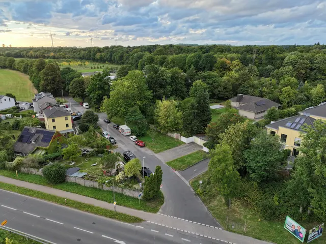 Das Bild zeigt eine Übersicht der Alten Aachener Straße. Rechts ist die Zufahrt zu den Klosterhöfen zu sehen. Auf dem Grünstreifen zwischen der Zufahrt zur Bauschule und der Einfahrt zu den Klosterhöfen. An der Stelle, an der aktuell Autos parken wird ein neuer Bürgersteig errichtet. | Foto: Tobias Weber