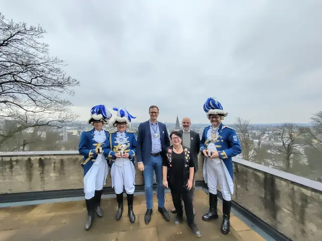 Zehnter Besuch der Funken Blau-Weiss beim KSI: Der mit dem Funkenorden geschmückte kommissarische Direktor des KSI André Schröder (3.v.l.), dem stellvertretenden Geschäftsführer Norbert Schramm (2.v.r.) und Birgit Meyer aus dem Direktionssekretariat (3.v.r.) zwischen den mit dem hauseigenen „Abtei-Fruchtaufstrich“ bedachten Blau-Weissen, Adjutant Klaus Stock (2. v.l.), dem 2. Schatzmeister Frank Breidenbach (l.) und Funkenoffizier Volkmar Johnen (r.).

 | Foto: Andreas Kaul, KSI