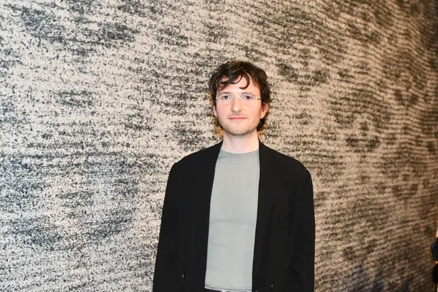 Der neue Max-Ernst-Stipendiat Fynn Ribbeck vor seinem wandfüllenden Teppich, dessen Muster an die wackeligen Bilder einer Überwachungskamera erinnert. | Foto: Foto: Brodüffel 