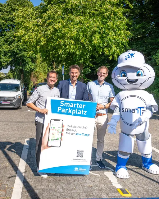 Projektleiter Max Schwerhoff (links), Bürgermeister Alexander Biber (2. von links), Stabsstellenleiter Fabian Wagner (2. von rechts) und das Digitalisierungsmaskottchen SmarTa.
