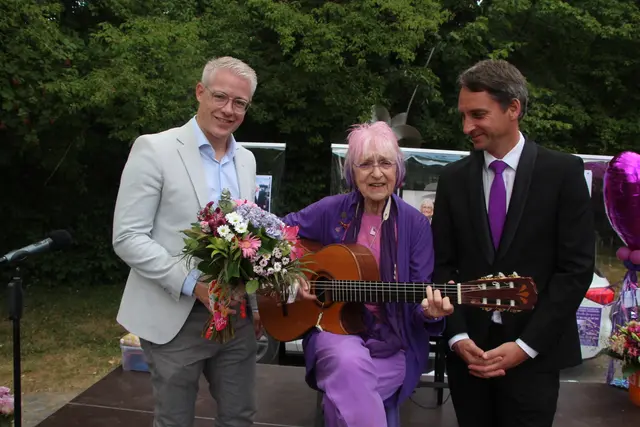 Jubilarin Monika Kampmann griff zu ihrem 80. Geburtstag natürlich auch selbst zur Gitarre. Bürgermeister Yannick Steinbach (l.) und Matthias Jaixen (r.) zählten zu den zahlreichen Gratulanten. Foto: Flick